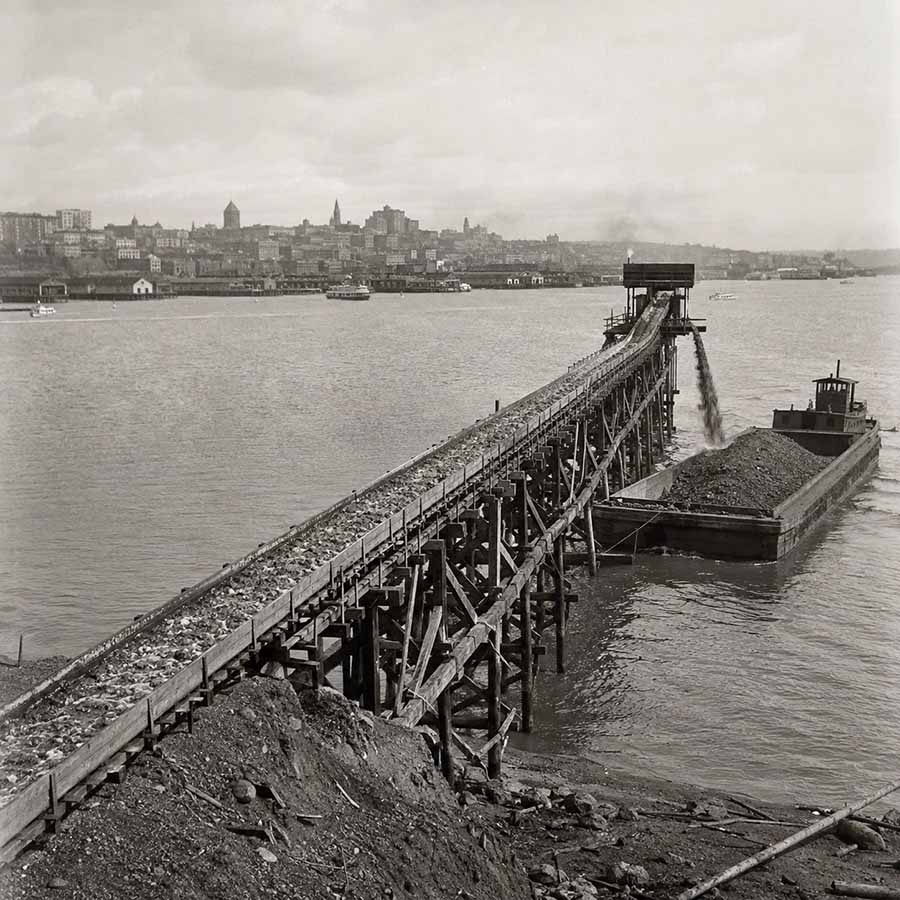 Elliott Bay waterfront history. A wooden flume stretching out into Elliott Bay on pilings, carrying sluiced earth from Denny Hill into the water below.